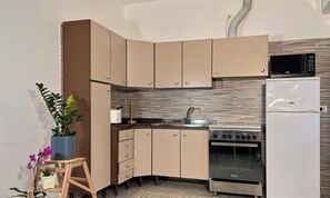 A compact kitchen with a microwave, stove, and refrigerator. - Residenza Nievo – apartment in Piazza Mazzini (Lido di Iesolo)
