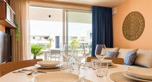 A dining area with a table set for four, a sofa with cushions, and a decorative wall piece. - OasiSole-Suite with Terrace and Pool (Lido di Iesolo)