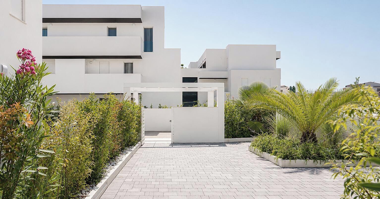 Edifici modern amb façana blanca, entrada enjardinada i vegetació circumdant.