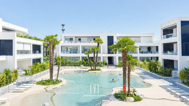 Un bâtiment moderne doté d’une piscine, de palmiers et surplombant un ciel dégagé.
