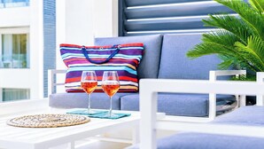 Un espace de détente extérieur moderne, avec un canapé, un coussin à rayures, deux verres de vin rouge et un set de table en fibres tressées.