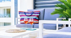 A modern outdoor seating area with a sofa, a striped pillow, two glasses of red wine, and a woven placemat. - OasiSole-Suite with Terrace and Pool (Lido di Iesolo)
