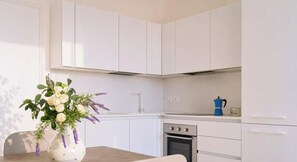 A modern kitchen with white cabinets, a stove, and a coffee maker. - SkyLux, 2-bedroom – 4th floor with view (Lido di Iesolo)