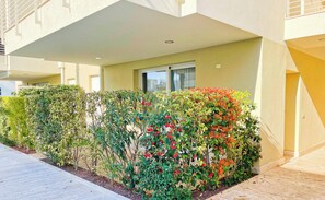 Ein Gebäude mit flachem Dach, einem Fenster und einer Hecke mit roten Blüten.