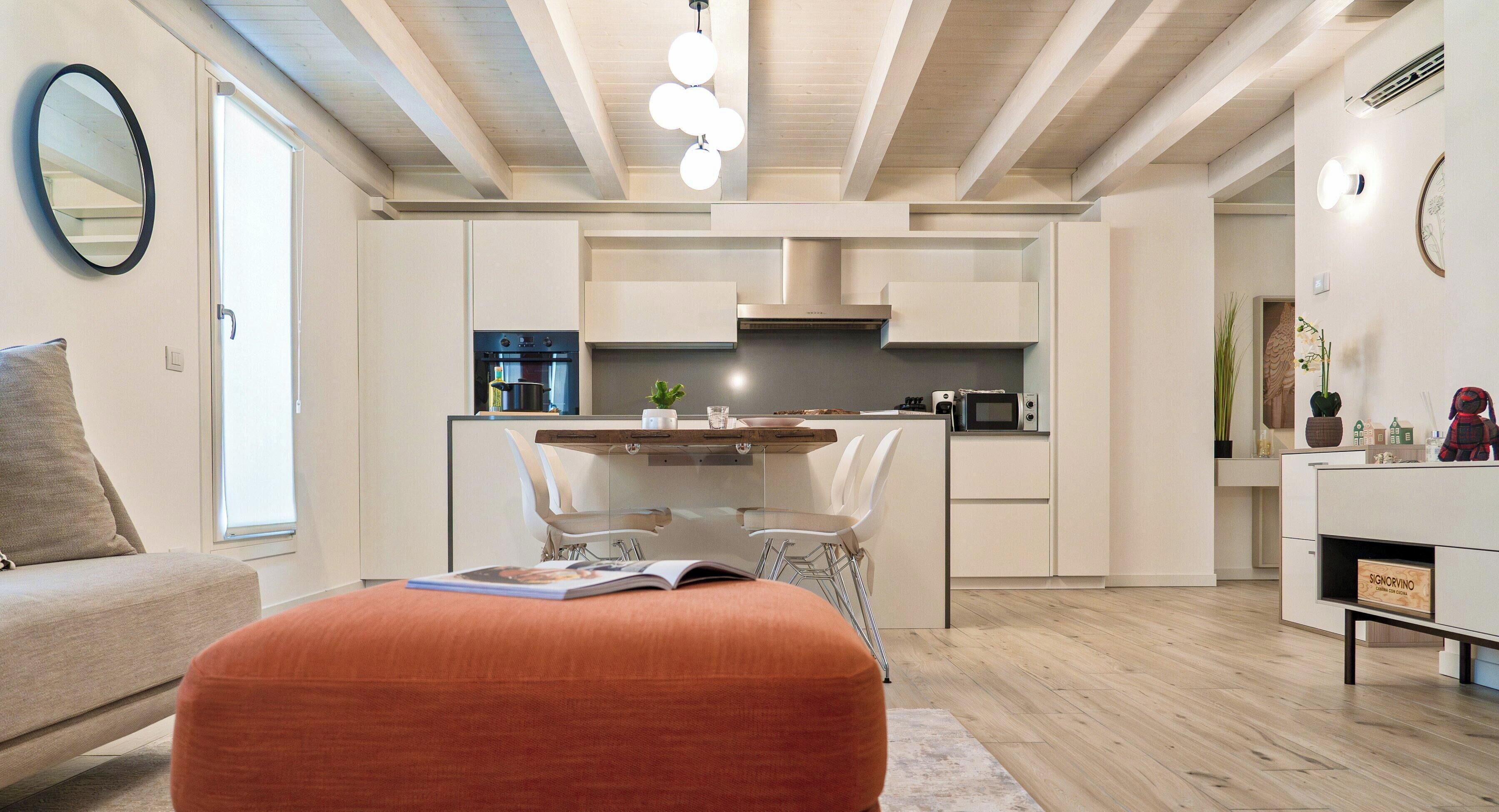 A modern kitchen with white cabinetry, a central island, and a dining area with chairs.
