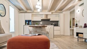 Een moderne keuken met witte kastjes, een centraal eiland en een eethoek met stoelen.