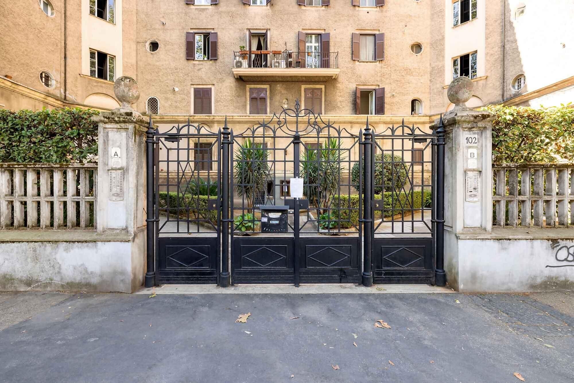 A gated entrance to a building with a wrought iron gate, a balcony with a railing, and a number plaque on the wall.