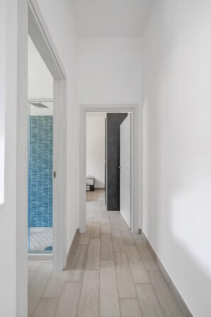 Ein Flur mit Holzboden, weißen Wänden und einem Badezimmer mit Duschkabine aus blauem Glas.