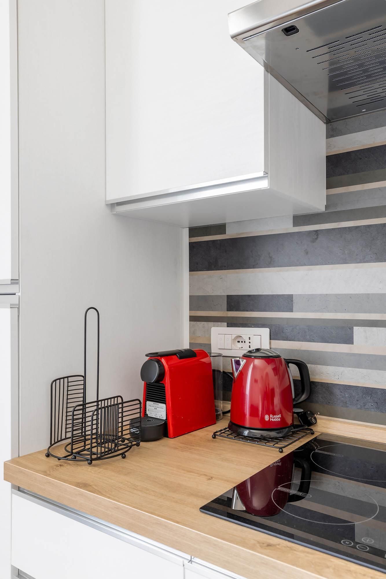 A modern kitchen with a built-in stove, a red coffee maker, and a black kettle.