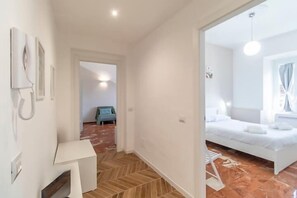 A hotel room with a bed, a small table, and a chair. There is a hallway with a door leading to another room. - Cocchina Residence (Roma)