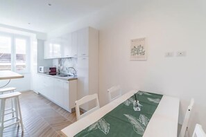 Eine moderne Küche mit weißen Schränken, einem Esstisch mit Tischdecke mit grünem Blattmuster und einem Fenster mit Blick.