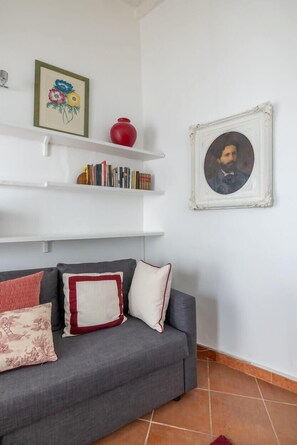 A grey sofa with patterned cushions, a red vase, and a framed portrait on a white wall. - Colosseum Charming Apartment (Roma)