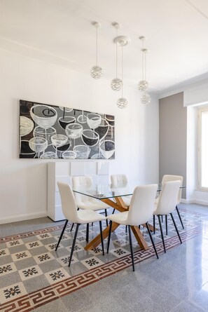 A dining area with a glass table, white chairs, a patterned floor, and a large abstract painting on the wall. - Coppedè Luxury Apartment (Roma)
