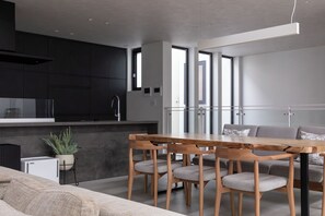 A modern kitchen with dark cabinetry, a wooden dining table, and a seating area with a sofa and chairs. - Entire Sapporo Villa | Private Sauna & Outdoor Bath | 10 Guests | 2 Free Parking (札幌市東区北２５条東２丁目)