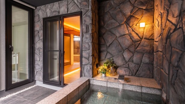 Ein Wellnessbereich mit Steinwand, Glastür zu einem Raum und einem kleinen Wasserspiel.
