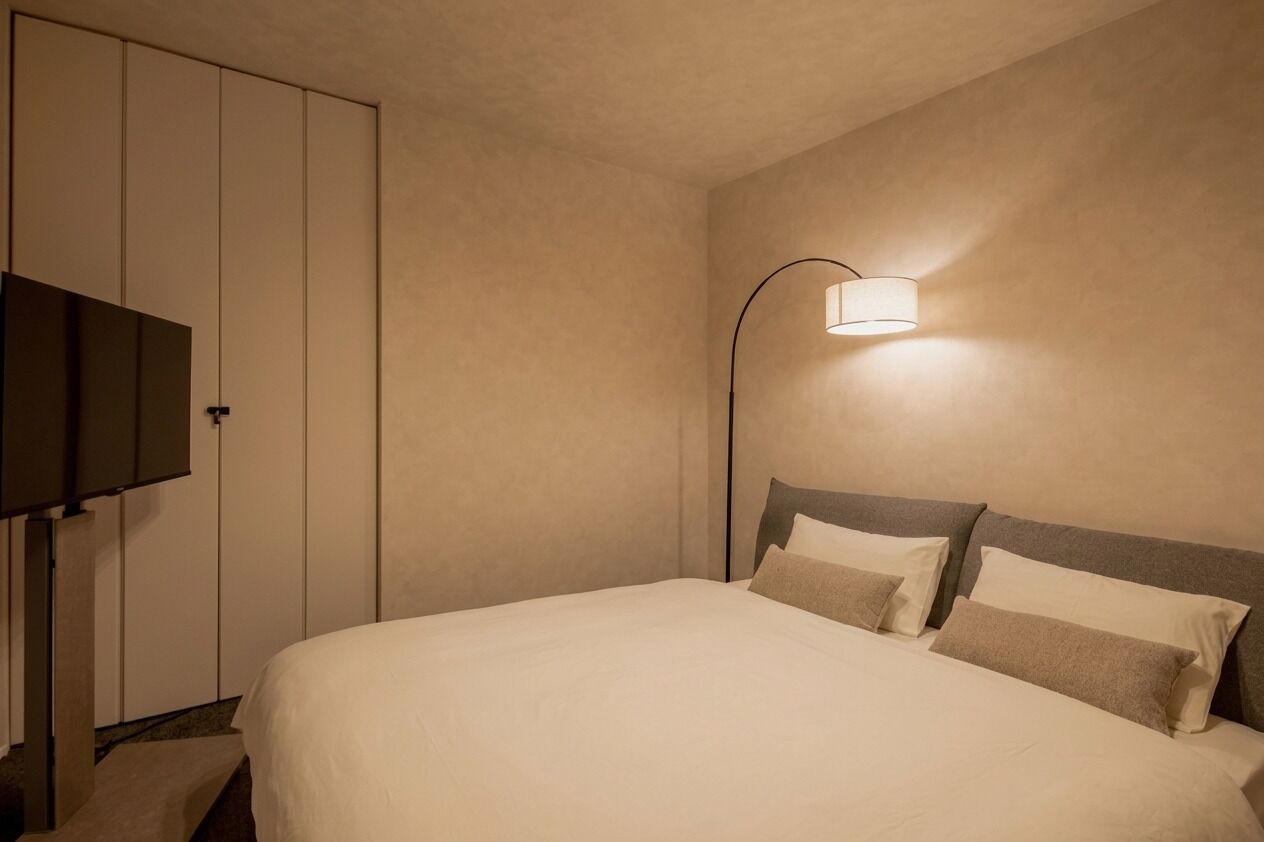 A hotel room with a bed, a TV, a wall-mounted lamp, and a wardrobe.