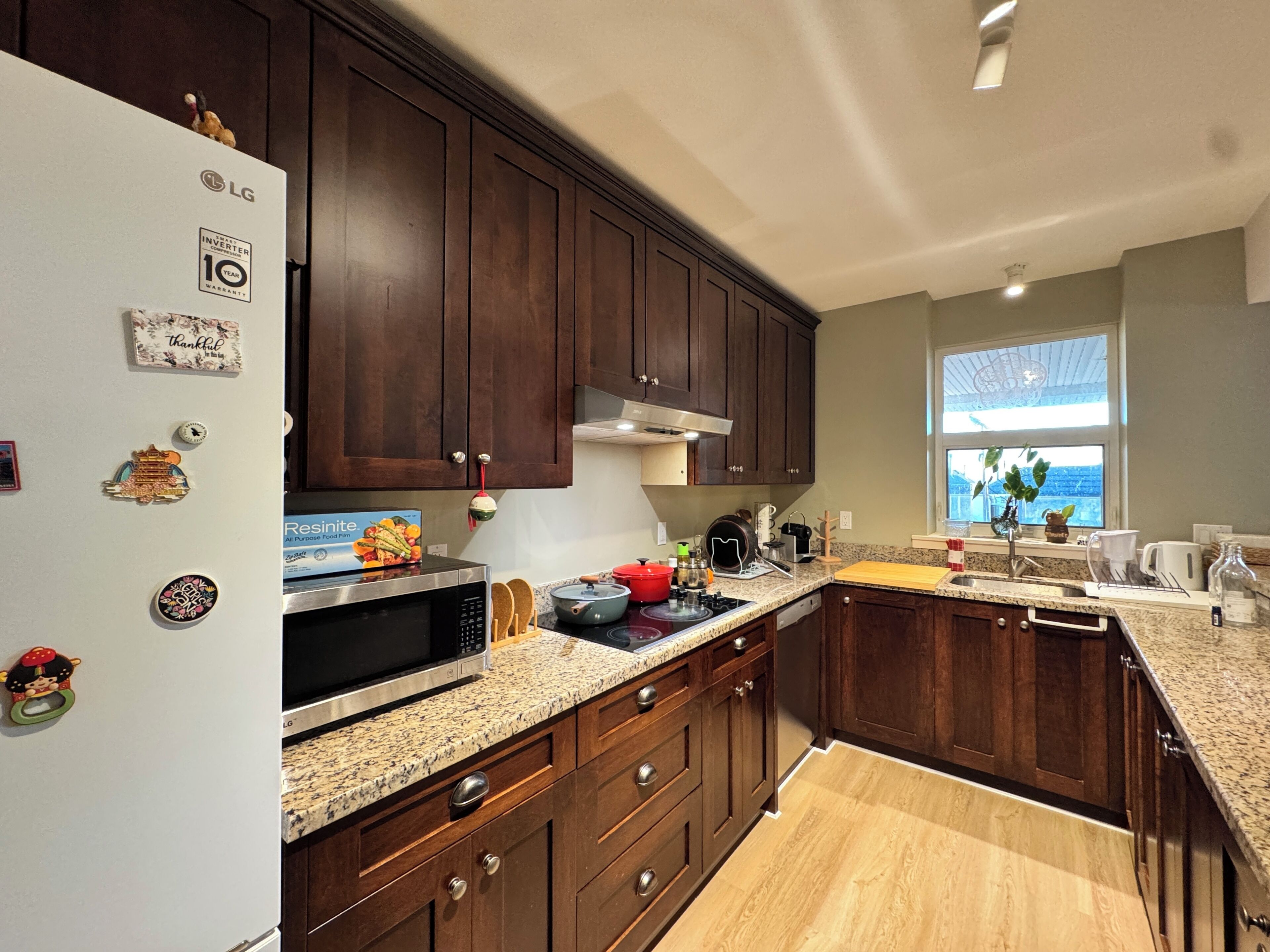 A modern kitchen with dark wooden cabinets, a white refrigerator, a granite countertop, and a window with a view.