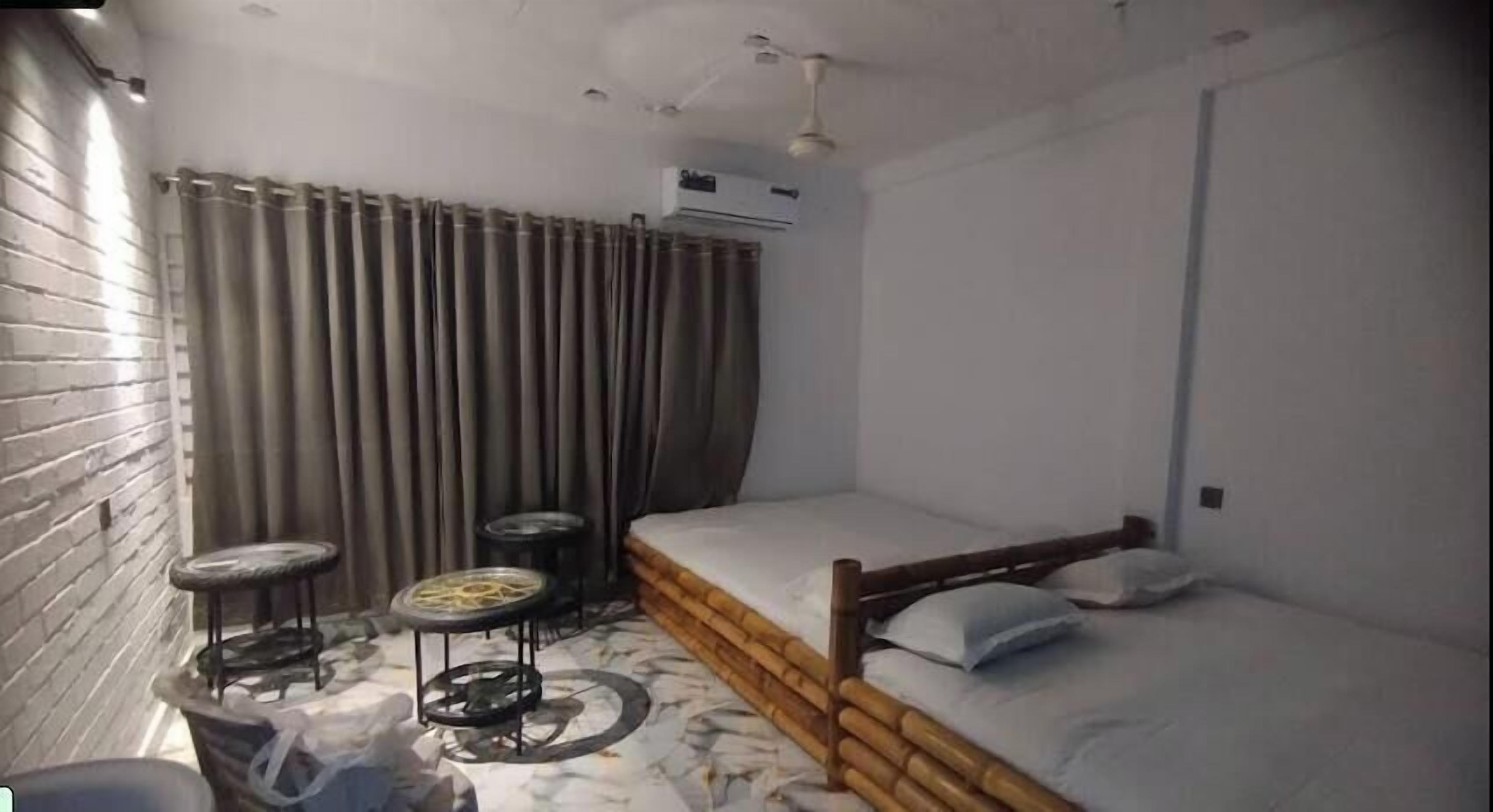 Una habitación pequeña con una cama individual, un taburete, una mesita y una cortina.