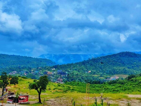 A rural landscape with a village, green hills, and a cloudy sky. - Hotel Jaflong Point (Gowainghat)