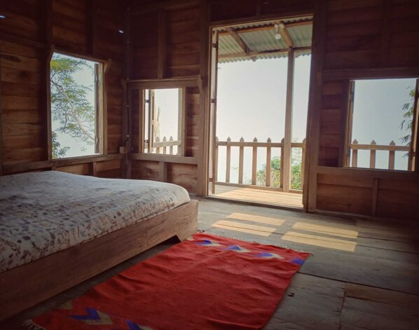 Dormitorio de cabaña de madera con cama, dos ventanas y un balcón.