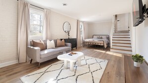En moderne stue med sofa, sofabord og en trappe til et soveværelse.