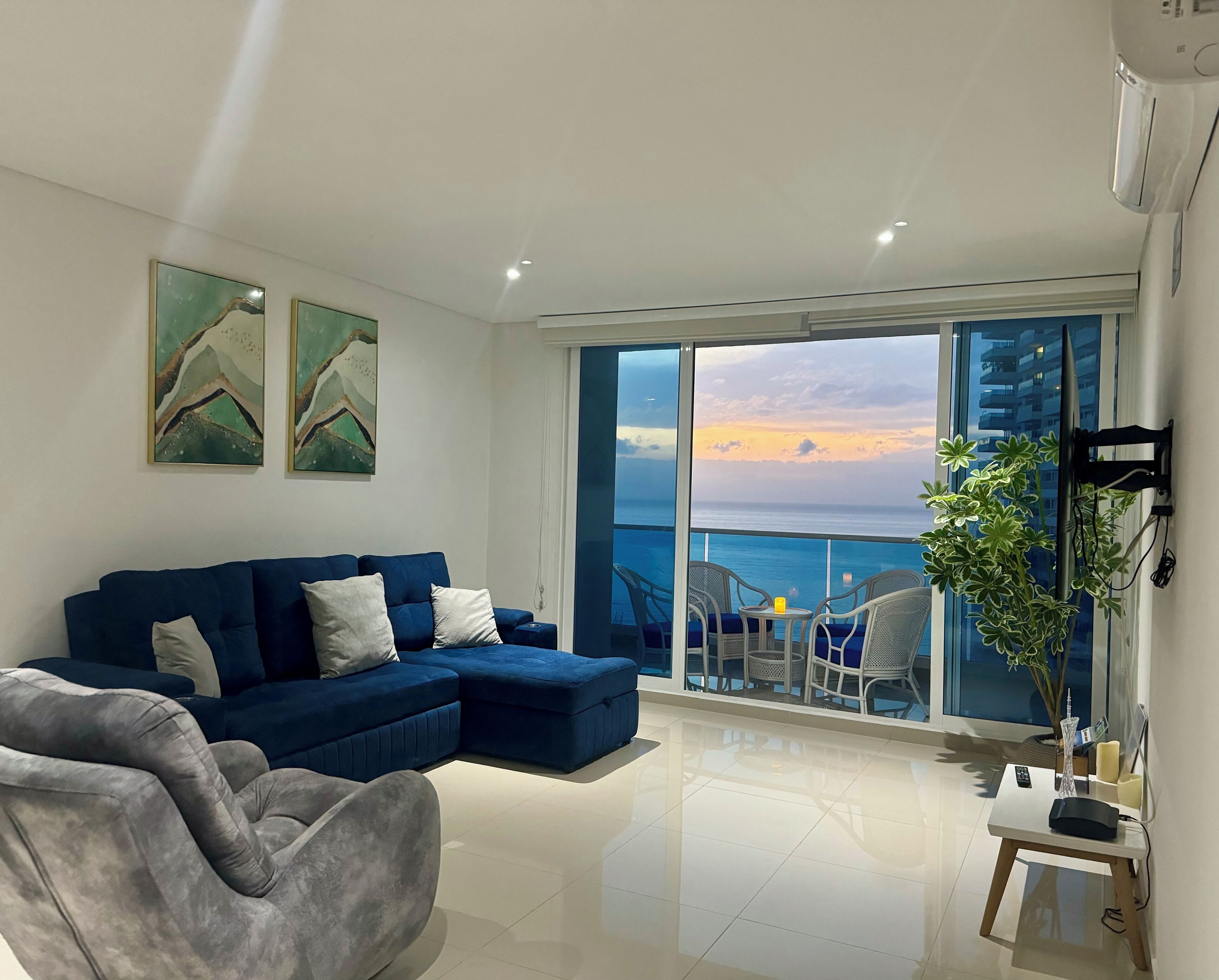 Een moderne woonkamer met een blauwe bank, een grijze fauteuil en een balkon met uitzicht op zee.