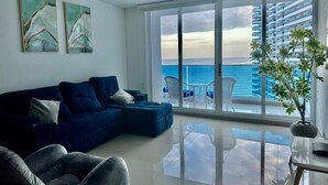 A modern living room with a blue sofa, a glass coffee table, and a view of the ocean through large windows. - Pleasant 1-bedroom apartment with AC in vibrant Rodadero (Rodadero)