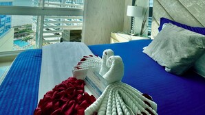 A hotel room with a large window, a bed with blue bedding, a red blanket, and a white towel. - Pleasant 1-bedroom apartment with AC in vibrant Rodadero (Rodadero)