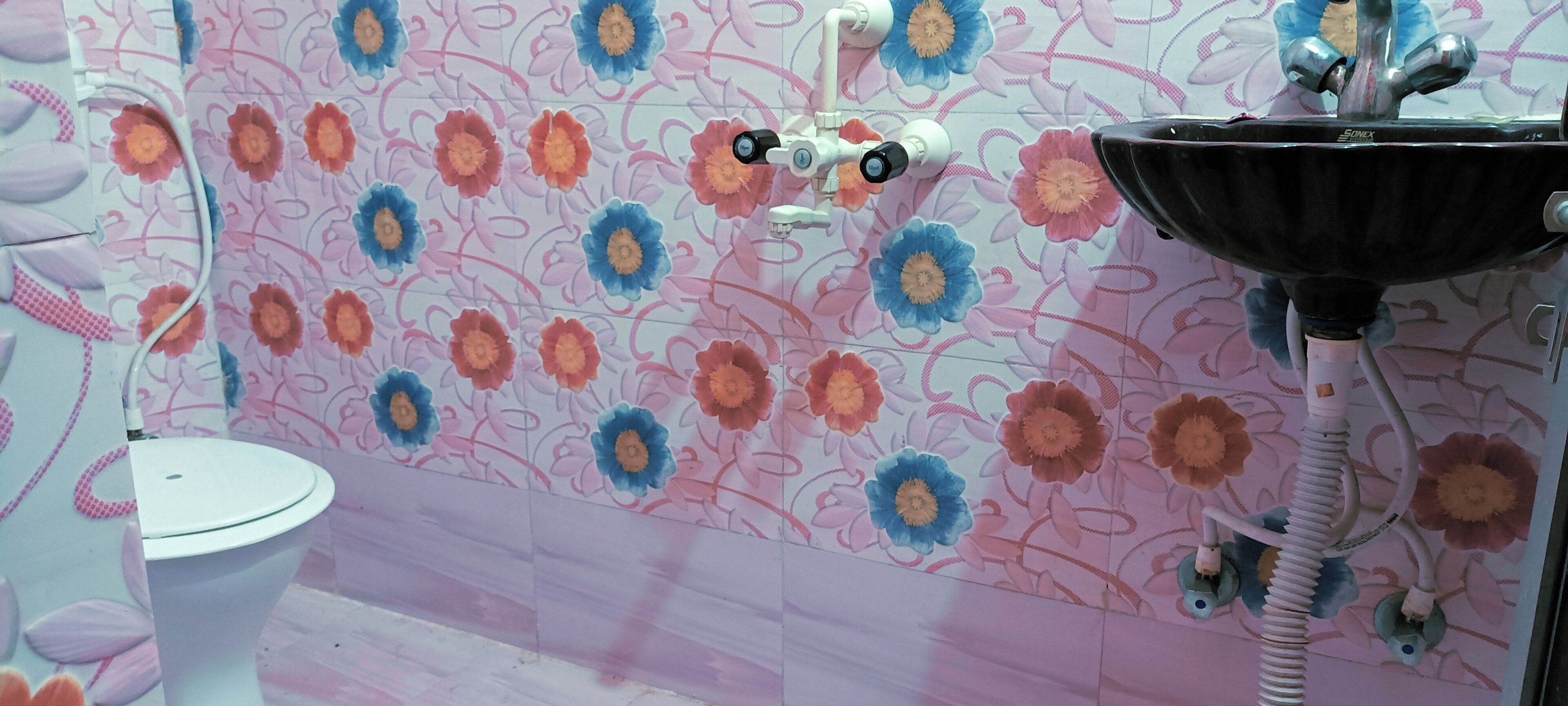 Et badeværelse med toilet, håndvask og brusebad med blomstermønstret væg.