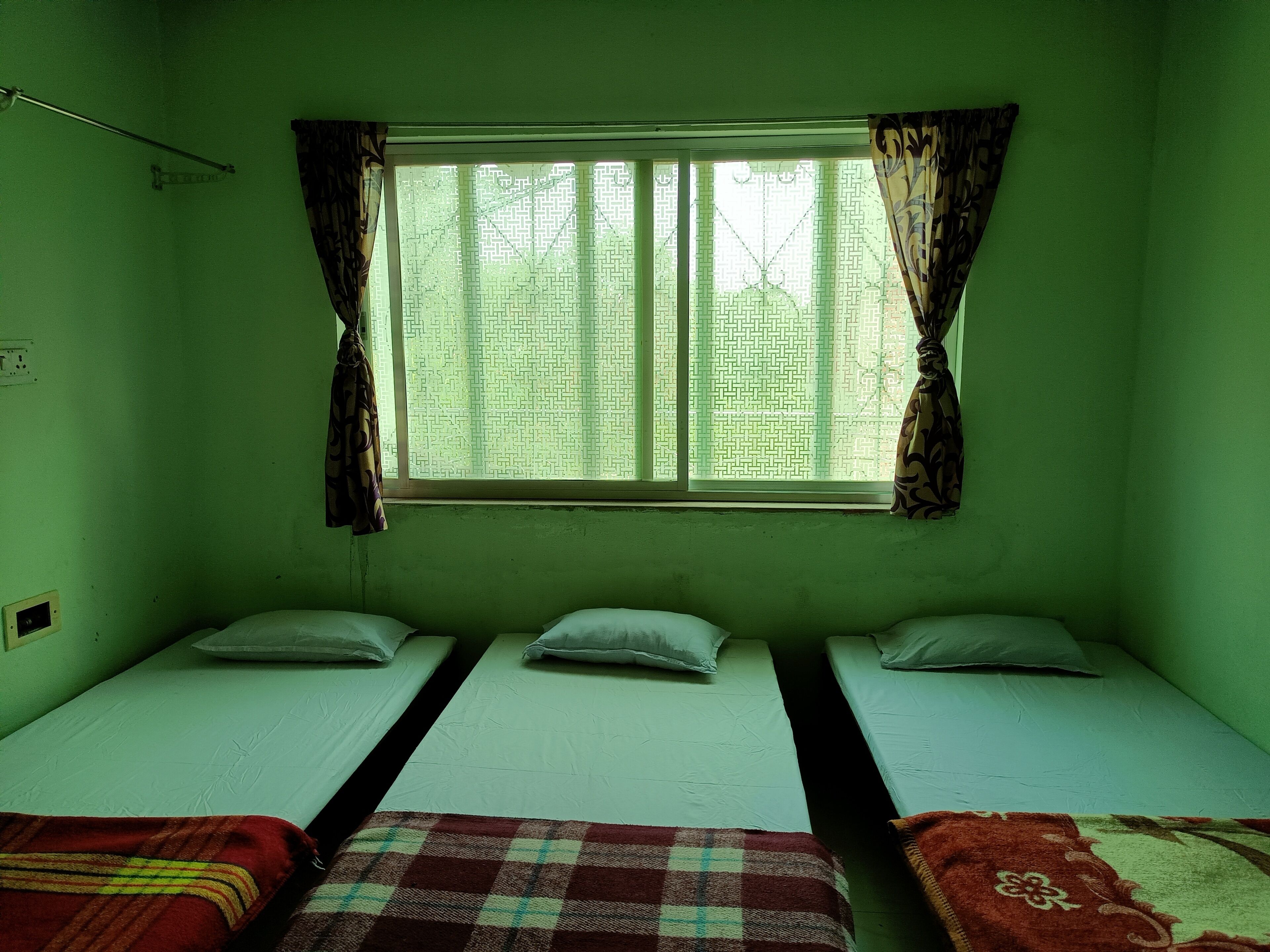 A room with two single beds, a window with patterned curtains, and a green wall.
