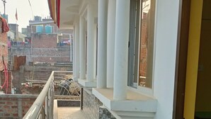 A corridor with a metal railing, a tiled floor, and a view of a brick building in the background. - MONIKA MANSION BODHGAYA (Bodh Gaya)