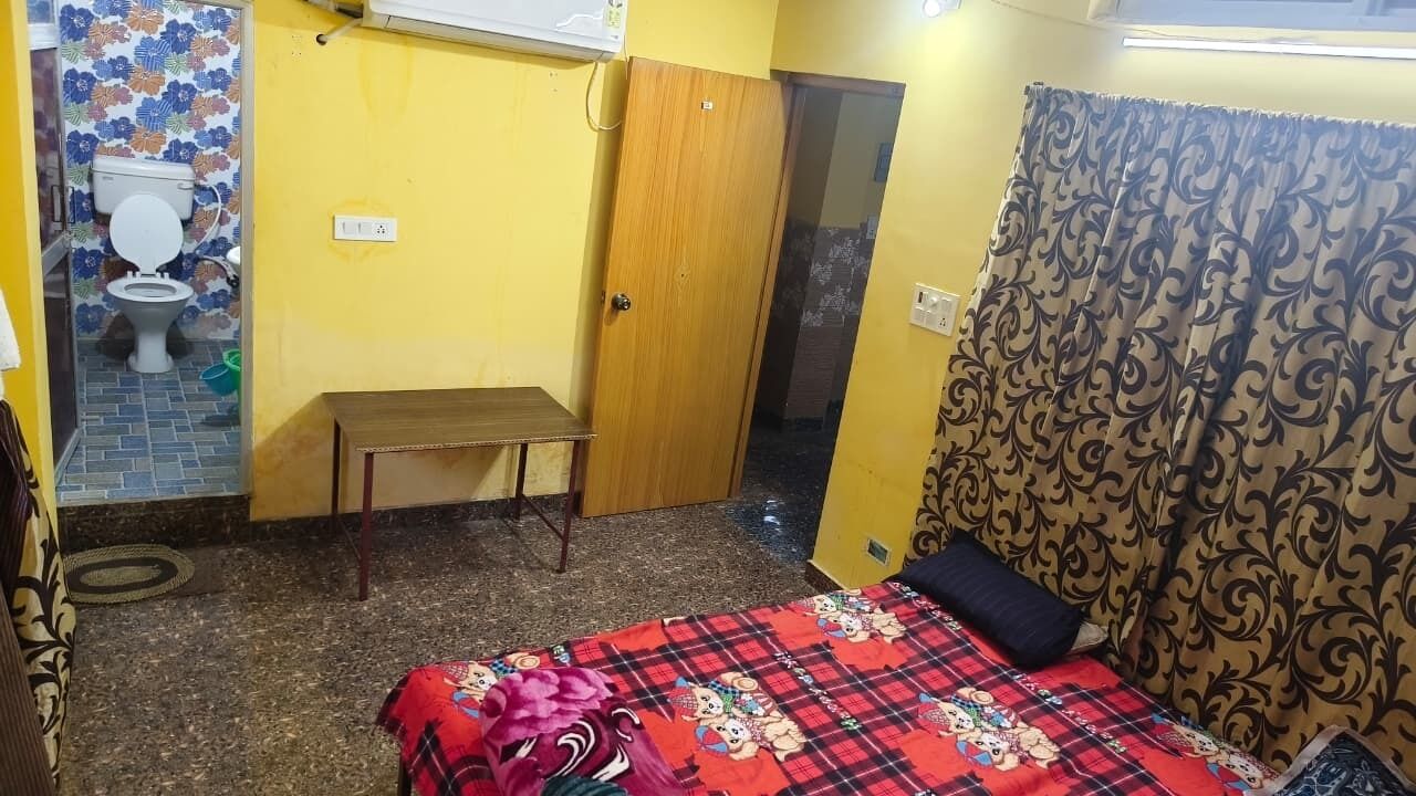 Una habitación pequeña con una cama, un banco, un inodoro y una puerta.