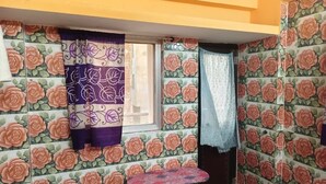 A room with floral wallpaper, a window with curtains, a small table, and a door. - MONIKA MANSION BODHGAYA (Bodh Gaya)