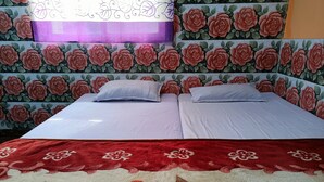 A double bed with white linens, two pillows, and a red floral blanket. The room has a floral wallpaper design and a purple decorative element above the bed. - MONIKA MANSION BODHGAYA (Bodh Gaya)