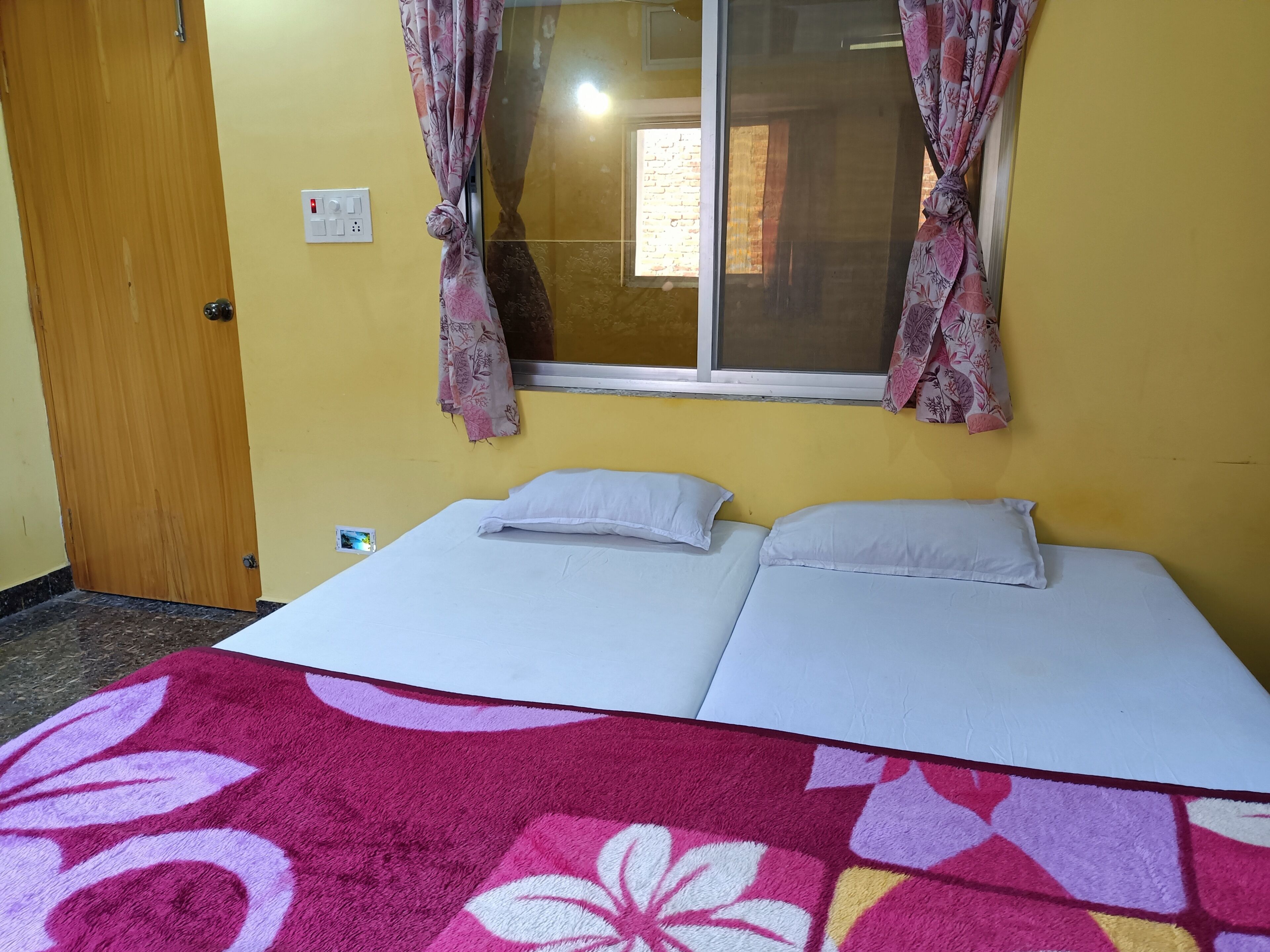 A room with a bed, a window with curtains, a door, and a wall socket.