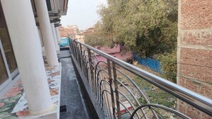 A balcony with a metal railing, a tiled floor, and a view of a brick building and trees. - MONIKA MANSION BODHGAYA (Bodh Gaya)