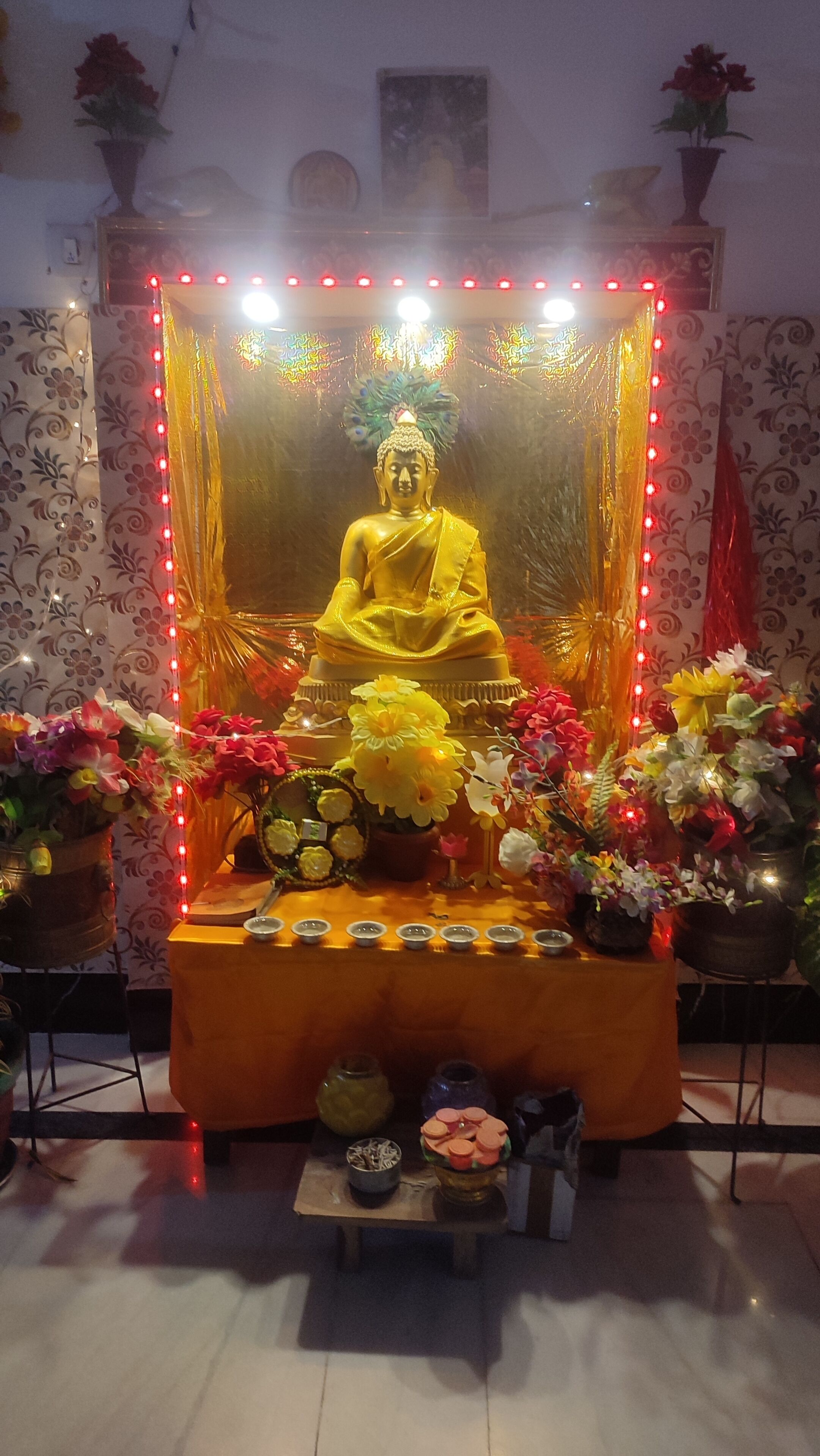 A statue of a seated figure surrounded by flowers and lit by red lights.