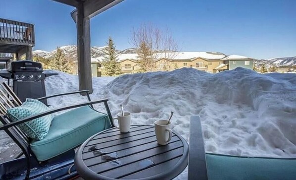 A patio with a table and chairs, a grill, and a snow-covered landscape with buildings in the background. - The Perfect Big Sky Getaway (Big Sky)