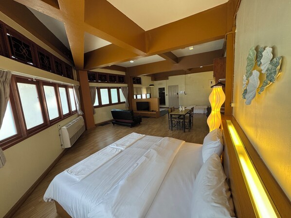 A hotel room with a large bed, a dining area, a TV, and a view through the windows.