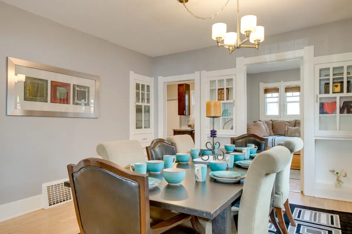 A dining area with a table set for four, chairs, a chandelier, and a view into another room.