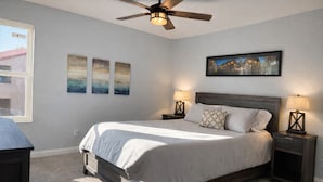 Quarto com cama, duas mesas de cabeceira com luminárias, um ventilador de teto e três quadros pendurados na parede.