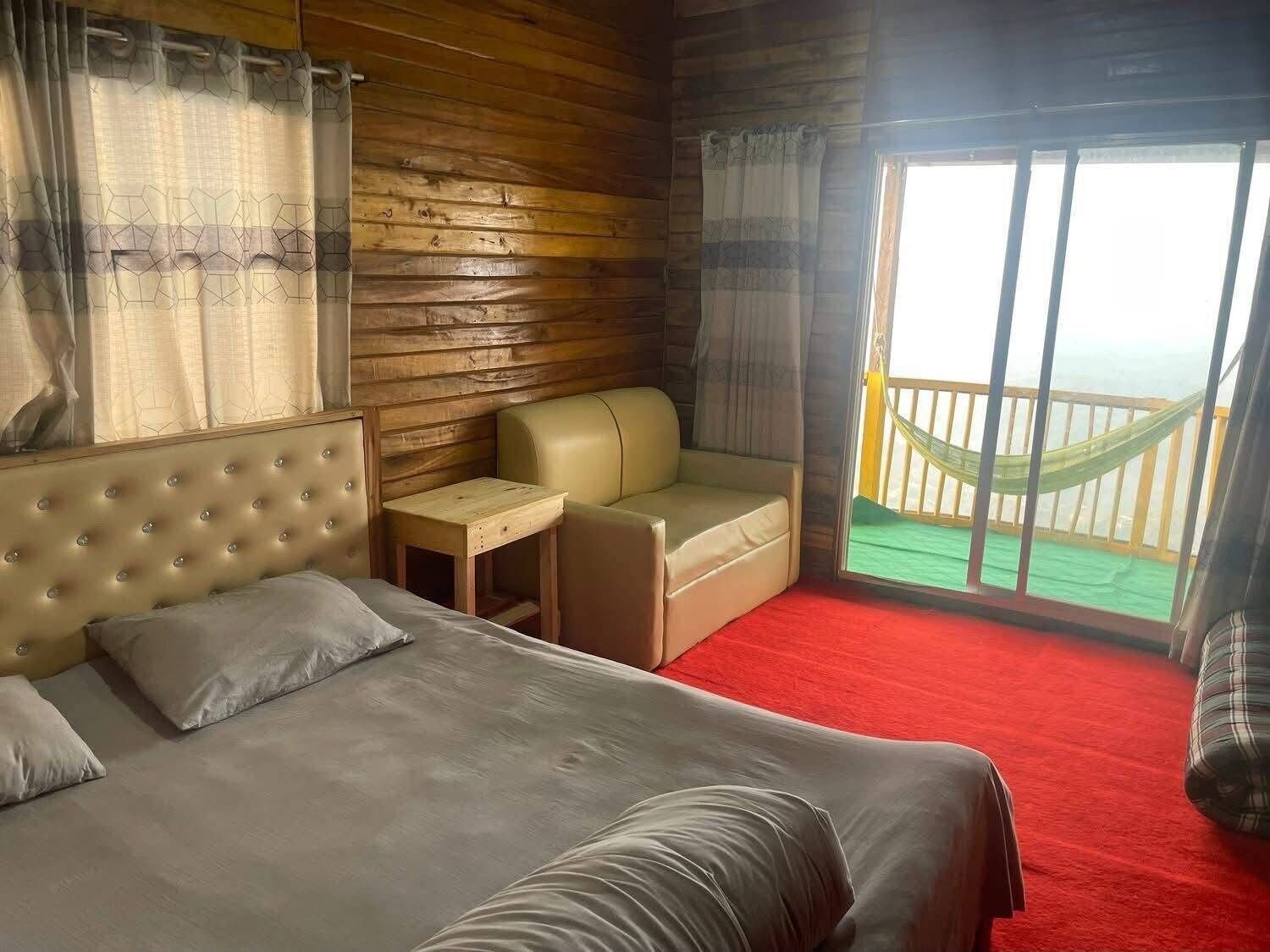 A room with a bed, a small table, a sofa, and a balcony with a hammock.