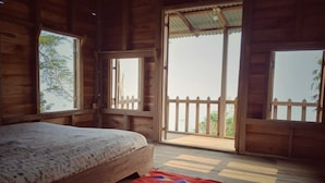 Una cabaña de madera con una cama, ventanas amplias y un balcón.