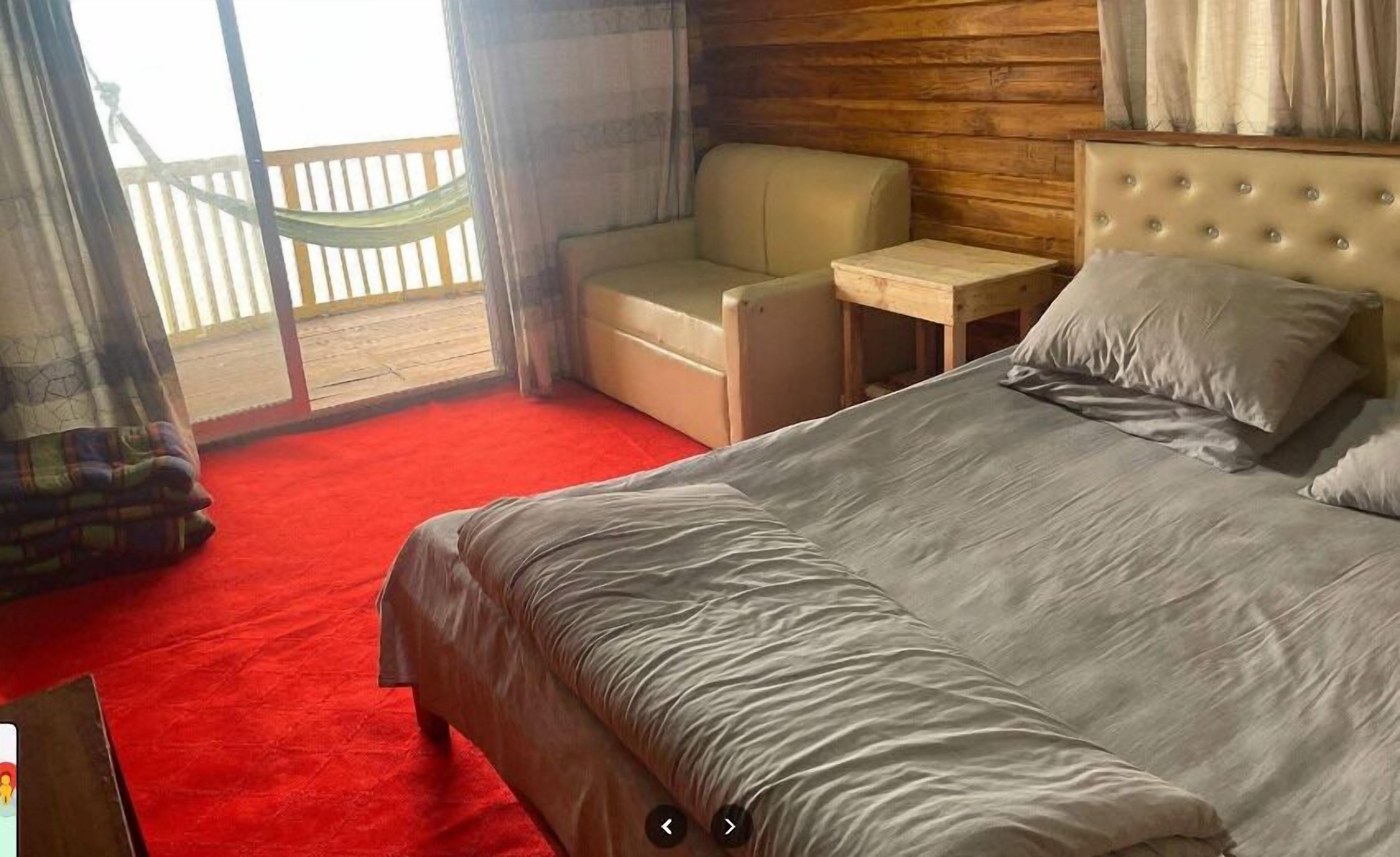 A bedroom with a large bed, a sofa, a small table, and a view of a wooden deck.