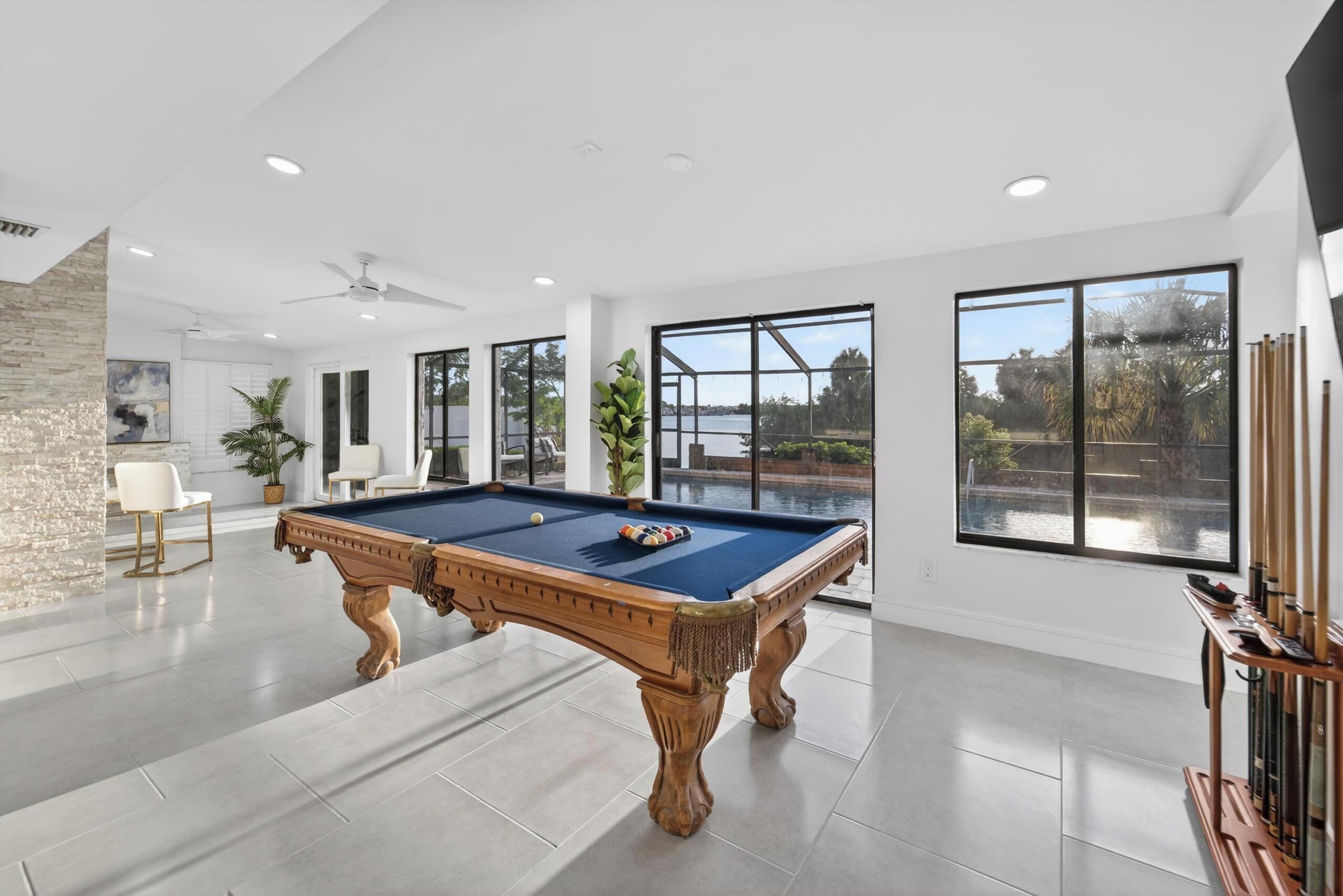 A pool table in a spacious room with large windows, a ceiling fan, and a view of a body of water.