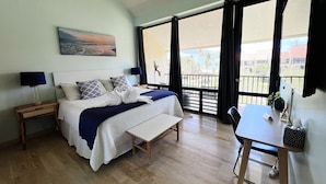 Un dormitorio con cama, mesitas de noche, escritorio, silla, ventilador de techo y balcón con vistas.