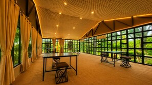 A spacious room with a high ceiling, large windows, and a long table with chairs.