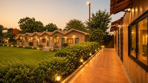 A row of modern, single-story hotel buildings with a well-maintained lawn and pathway. - blue heaven resort jaipur  (Jamwa Ramgarh)
