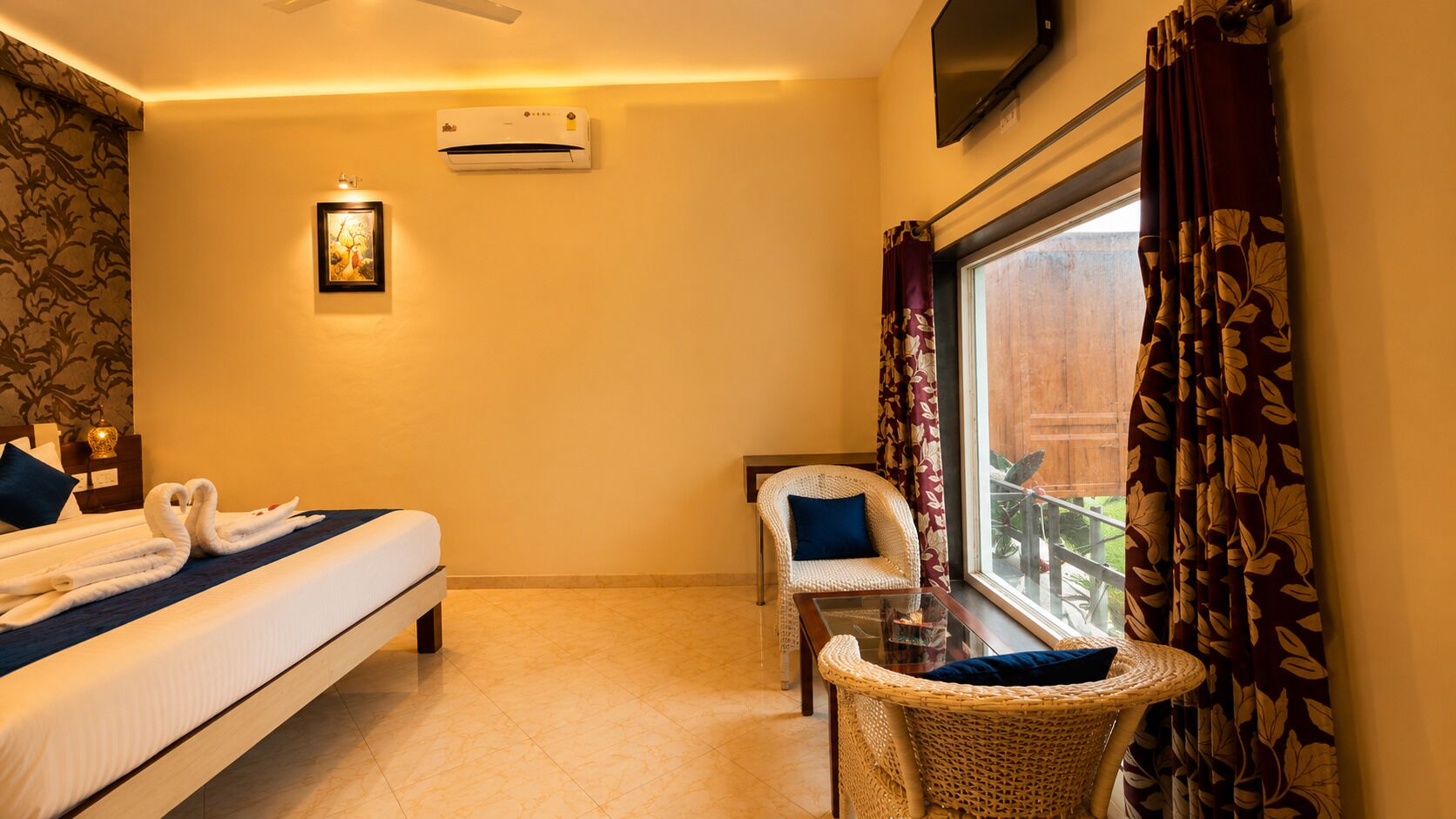 Ein Hotelzimmer mit Bett, Sessel, kleinem Tisch, Klimaanlage, Fernseher und einem Fenster mit Vorhängen.