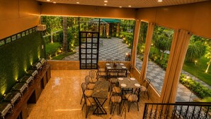 A restaurant with outdoor seating, a checkered floor, and a view of a garden. - blue heaven resort jaipur  (Jamwa Ramgarh)